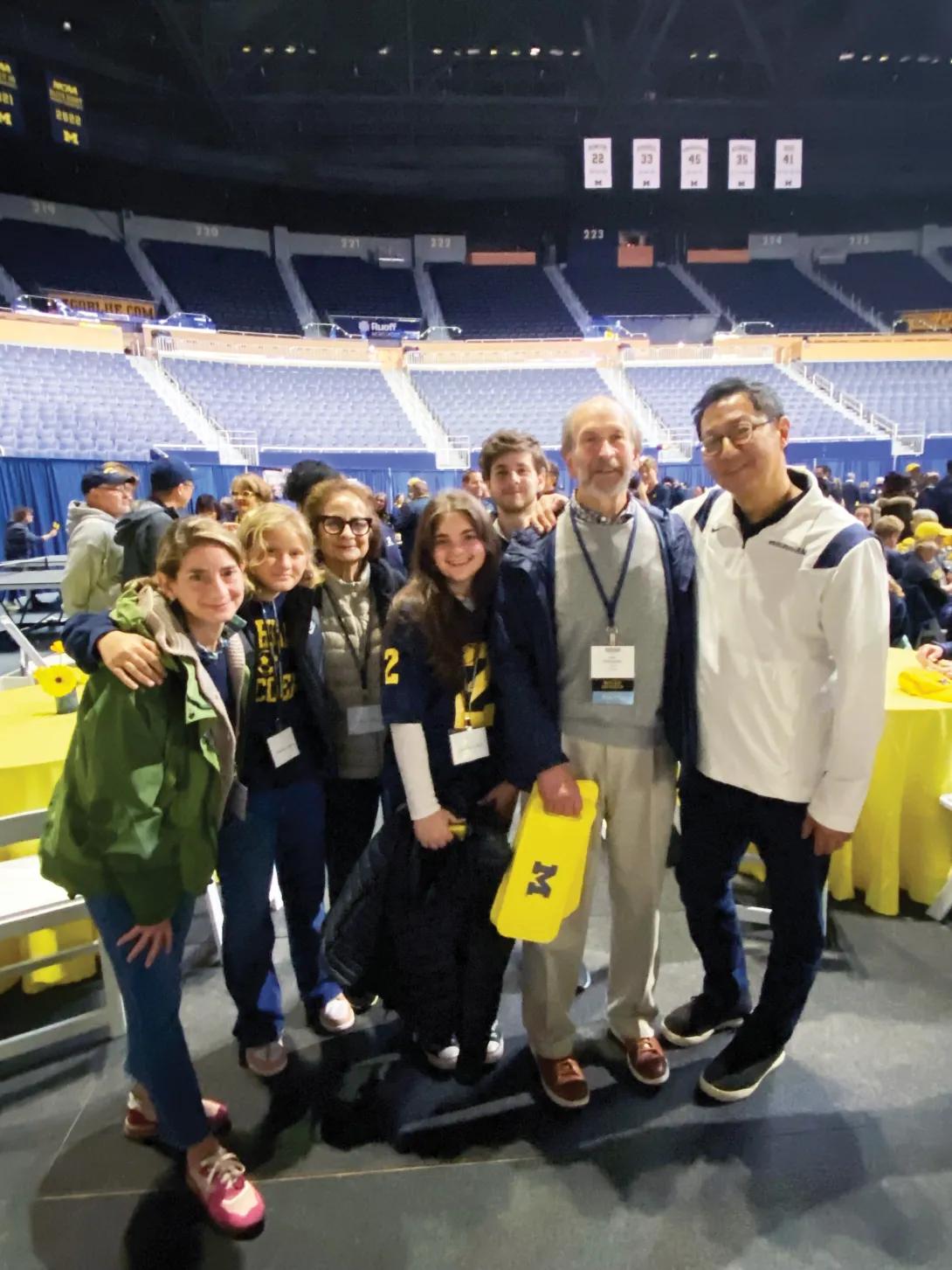 Group of people, including U-M president Santa Ono, standing and smiling at an alumni pregame celebration.
