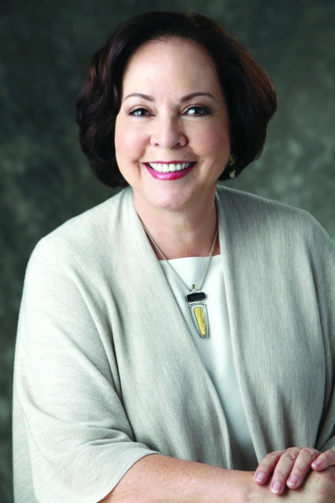 Headshot of Carolyn Ross. She's wearing a light green shawl with a white shirt underneath and a pendant necklace.