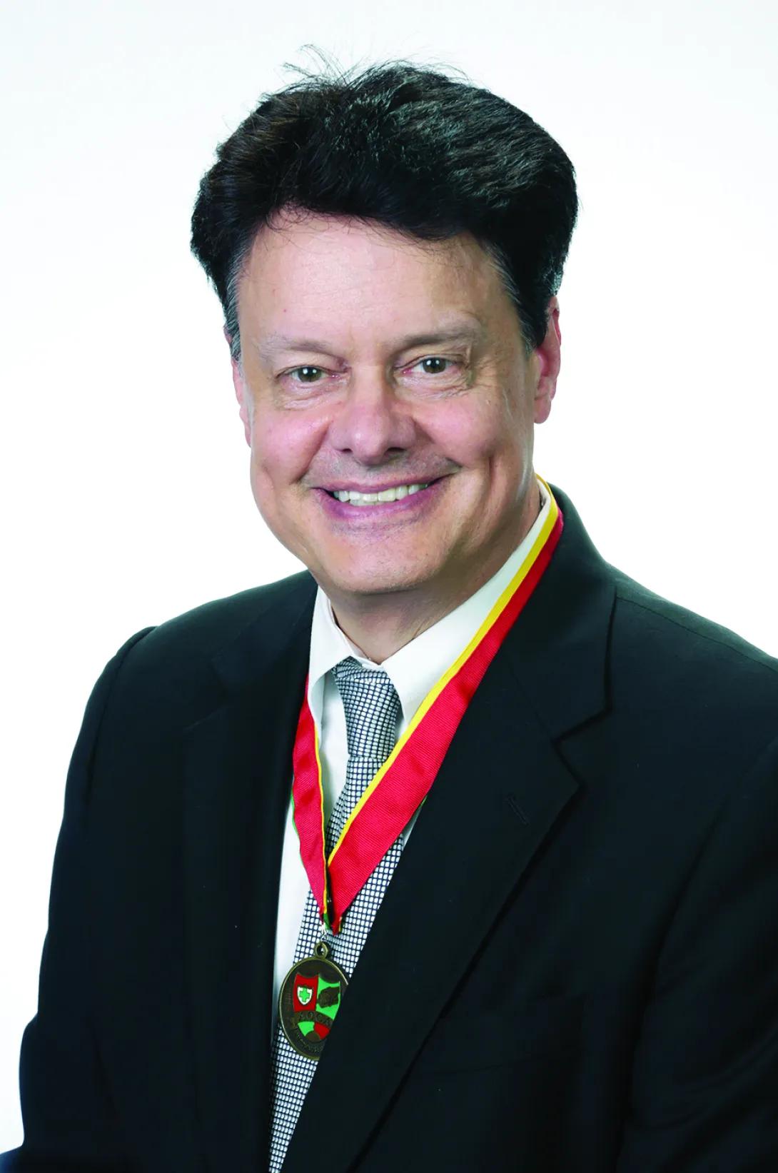 Headshot of Allen Escher. She's wearing a suit and has a medal around his neck.