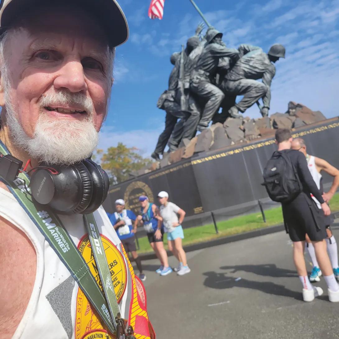 Man wearing headphones standing in front of a war memorial statue. 
