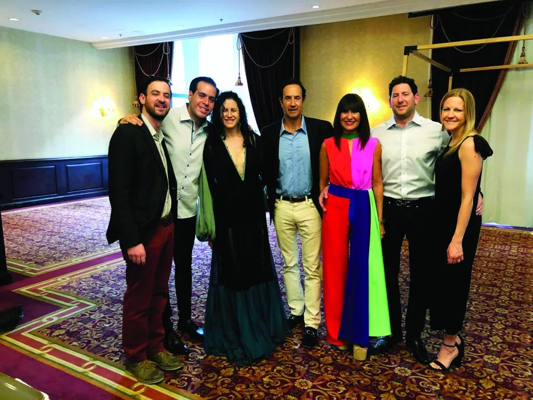 Seven people standing smiling at the camera. It looks like they're at a fancy event. 