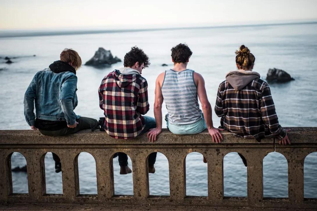 Group of young people sitting on guardrail near a river.
