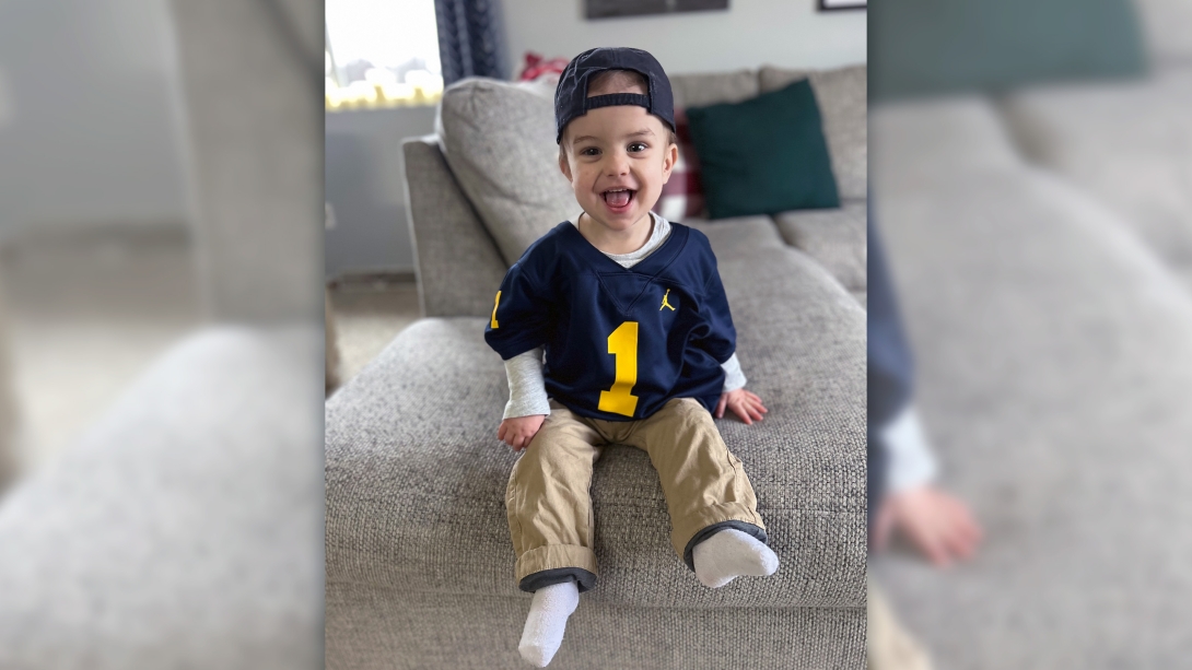 Smiling toddler sits on a couch in a University of Michigan jersey