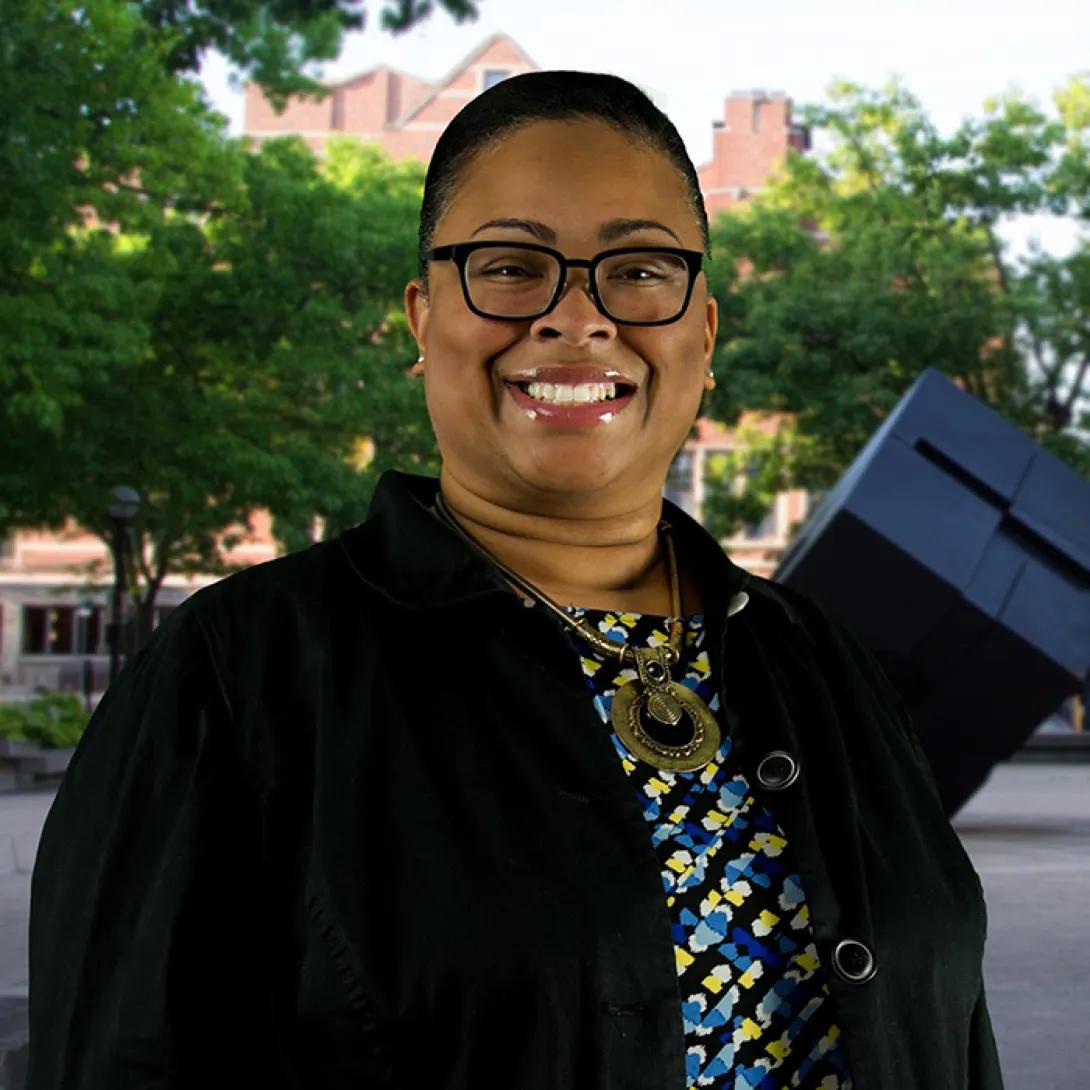 Smiling Black woman wearing glasses, a print shirt and black with U-M Cube in the background