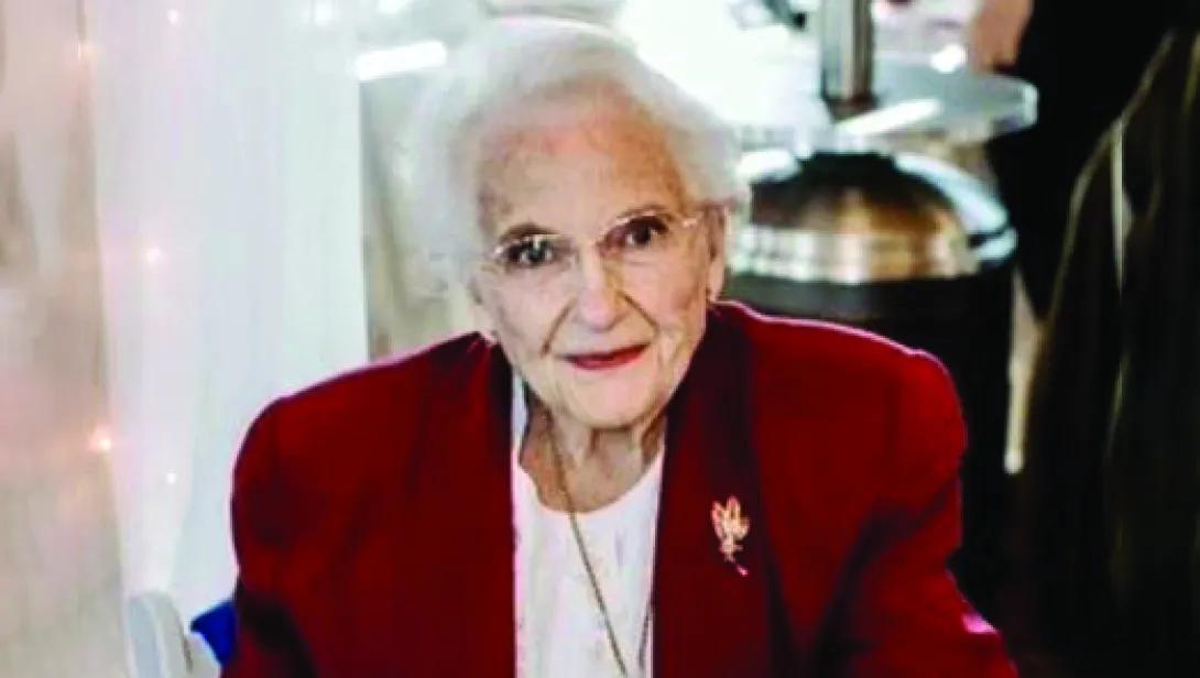 Marguerite Shearer is an elderly woman with short white hair. She's wearing a red jacket and white shirt.