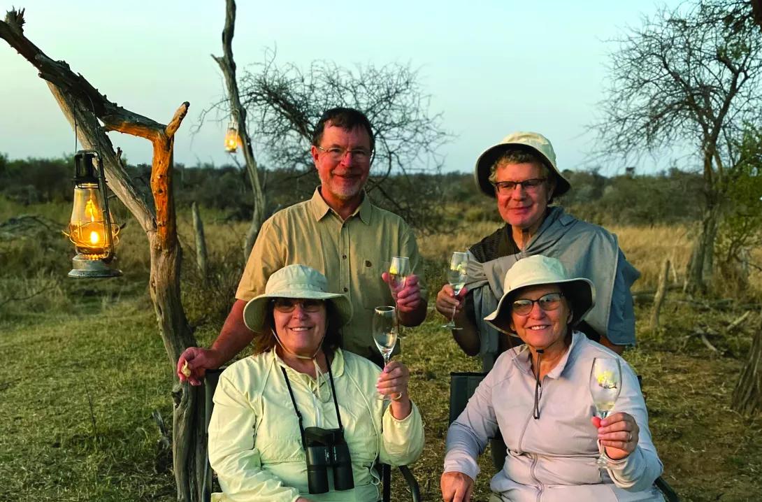 Four people holding wine glasses. They're sitting outside and there are lanterns hanging in the trees.