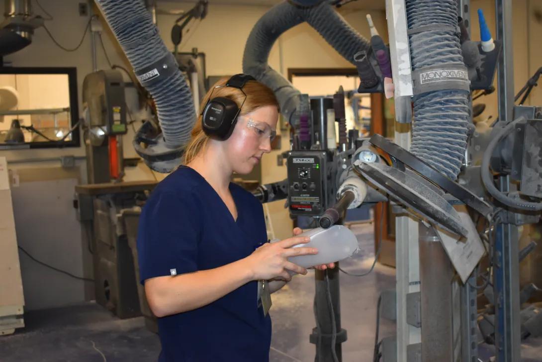 woman working on prosthetic in clinic with machinery around wearing black headphones