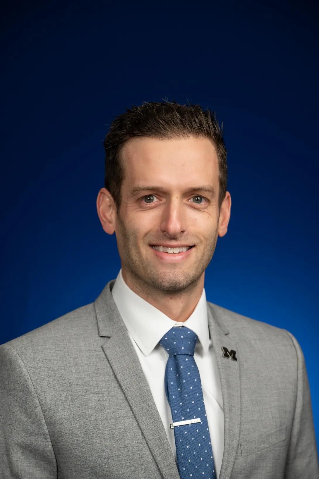 Smiling headshot of Mike Blanchette wearing a light gray jacket and blue tie.