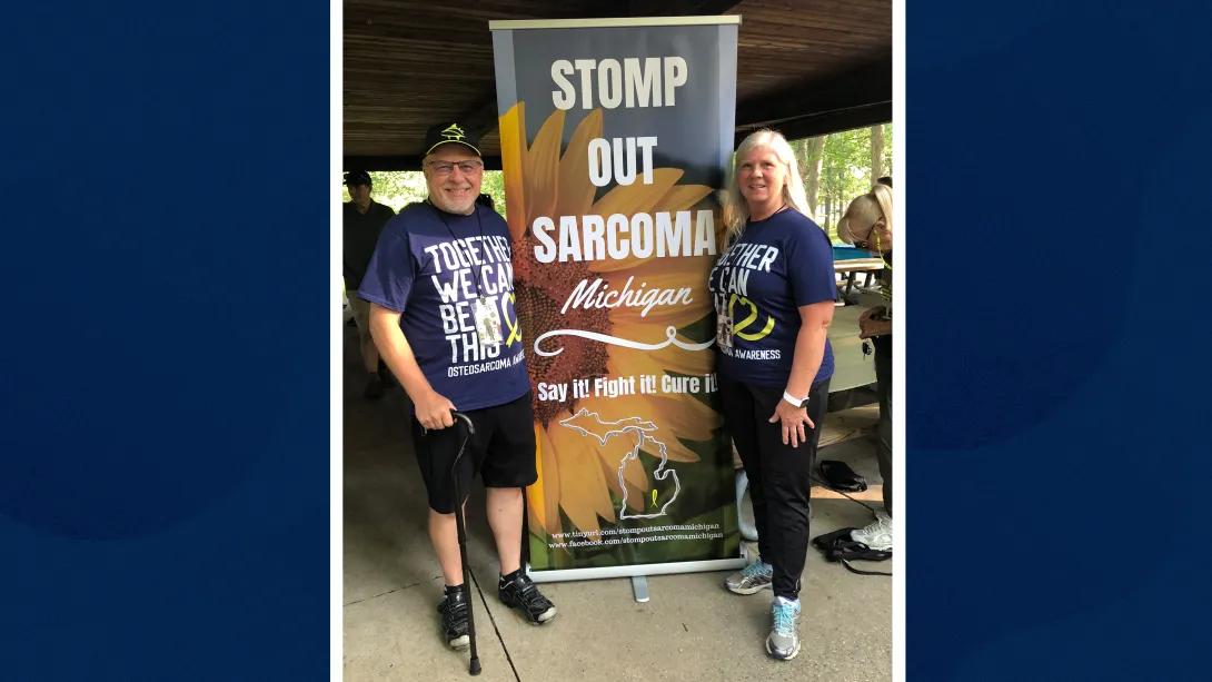 man and woman standing infront of sign that says stomp out sarcoma