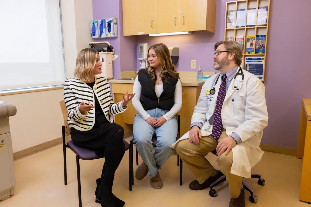 woman sitting talking with coworkers sitting in exam room with purple walls and light wood cabinets