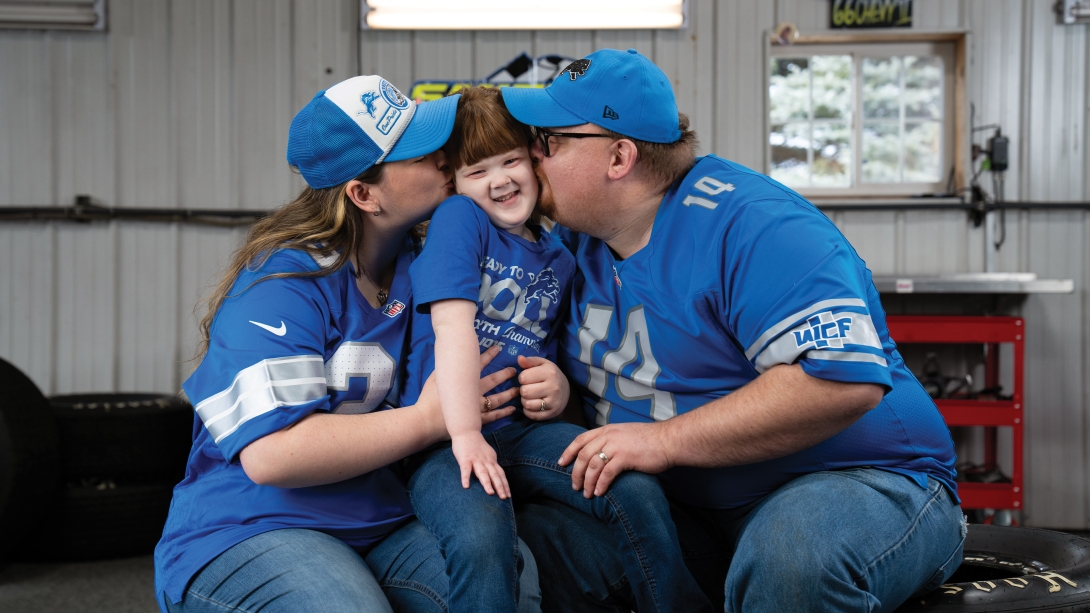 two parents kissing kid in middle all in blue and blue hats