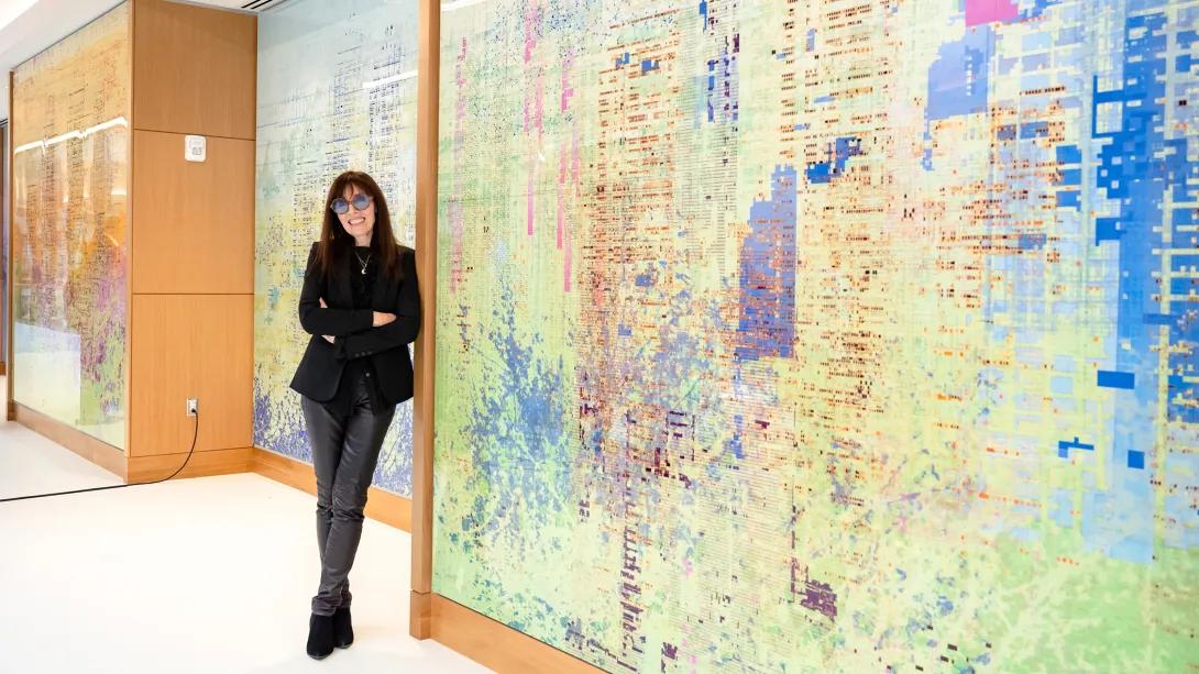 artist in black standing in front of huge mural artwork light green blue purple pink 
