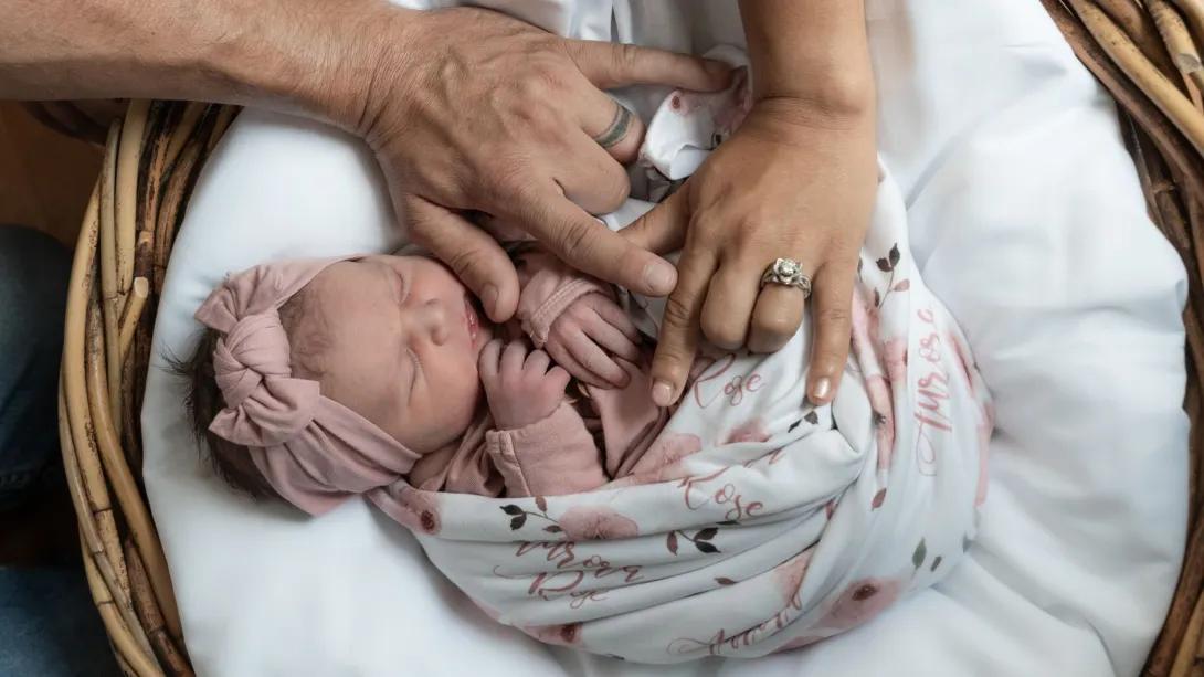 baby close up with each parent's hand on the baby bundled up in blanket in a basket