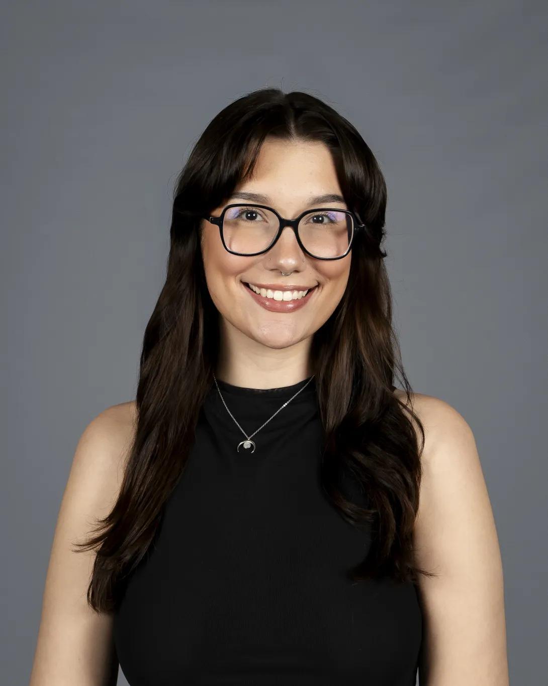 A photo of Arianna Mullen, who describes herself as having brown eyes, pale skin, brown hair, and black glasses 