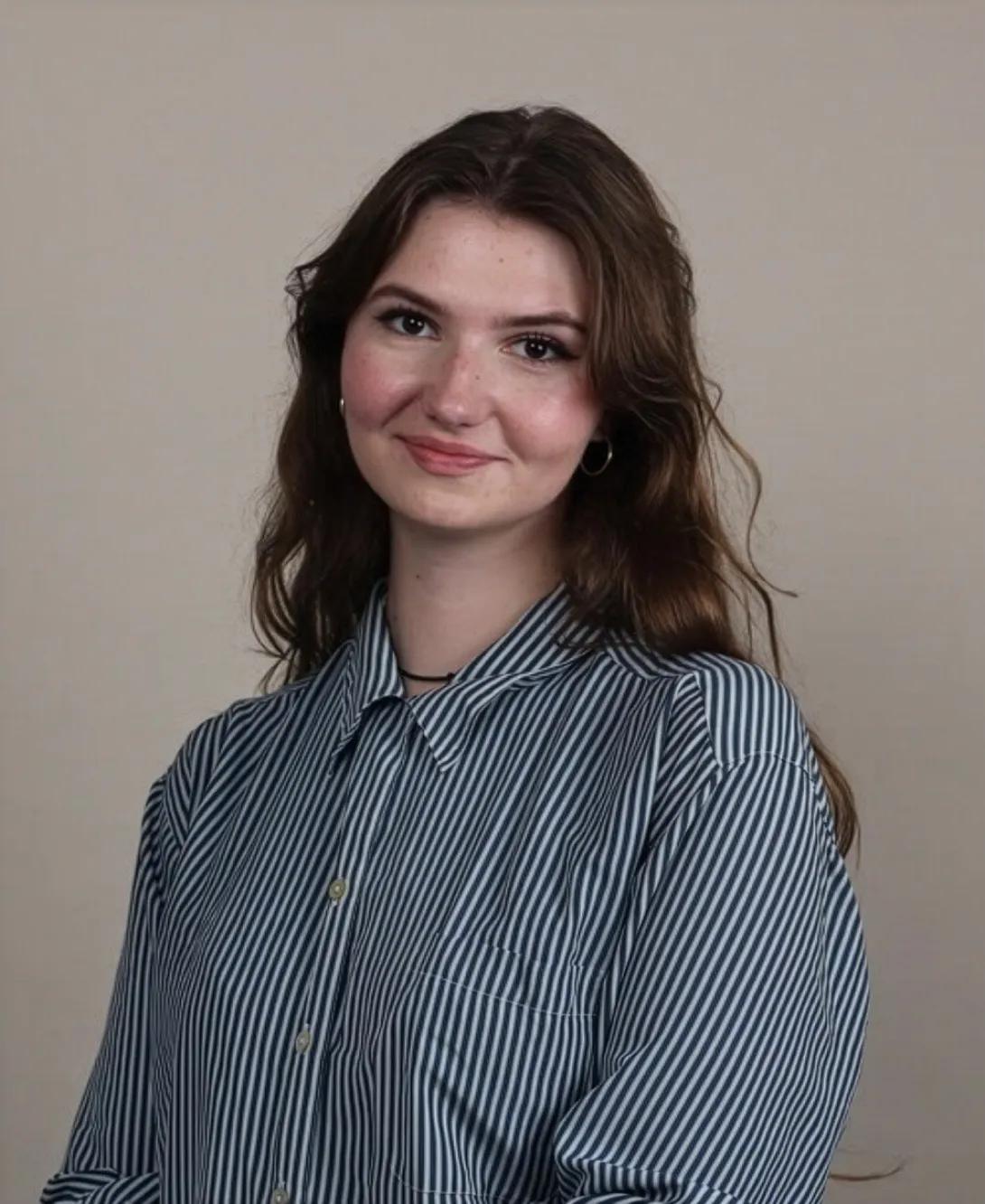 A photo of Mia Echlin wearing a striped blue shirt in front of a beige background.
