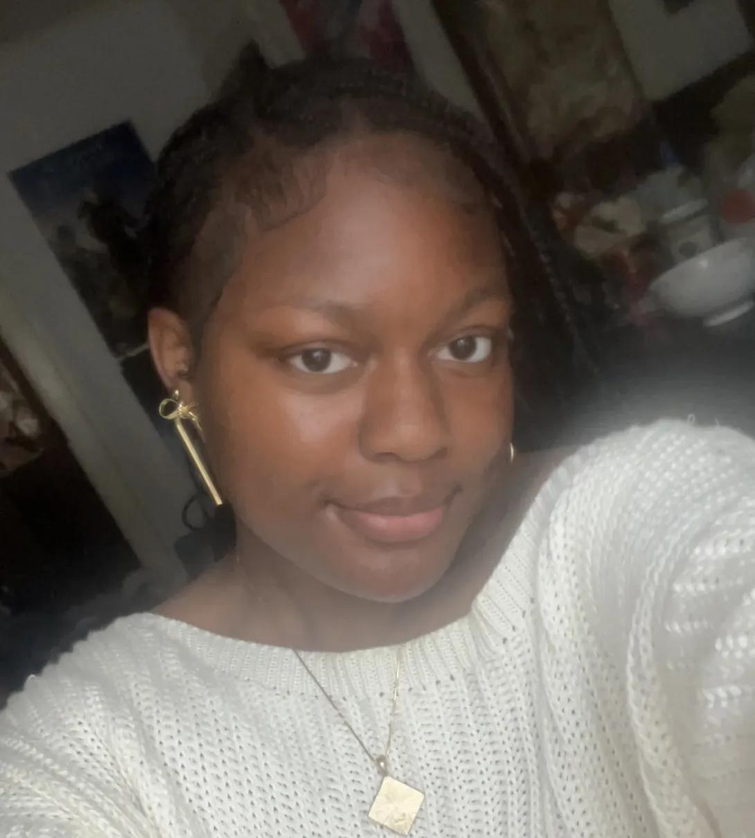 A photo of Simone Sumpter wearing a white sweater and gold earrings and necklace.