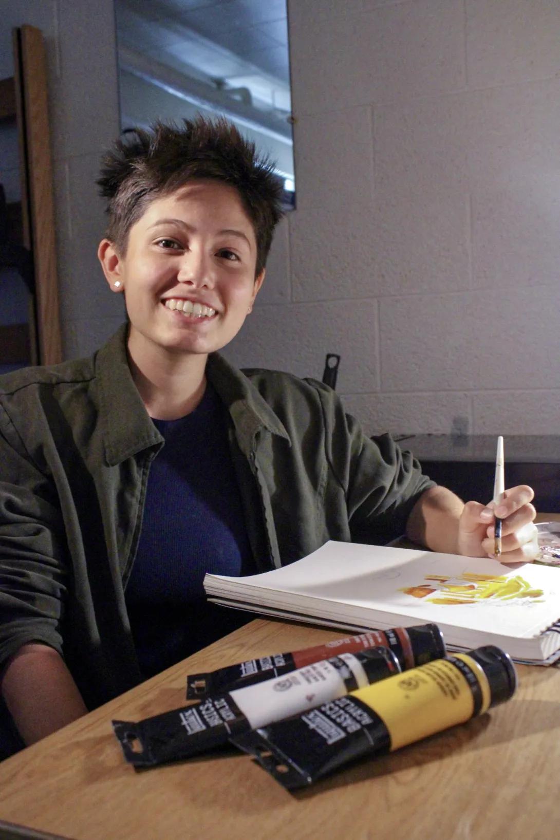 A photo of Sof Berlanga seated at a table with art supplies.