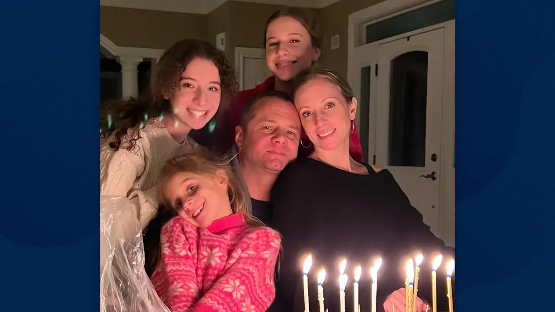 Man, woman and three young girls pose in front of a birthday cake lit with candles.
